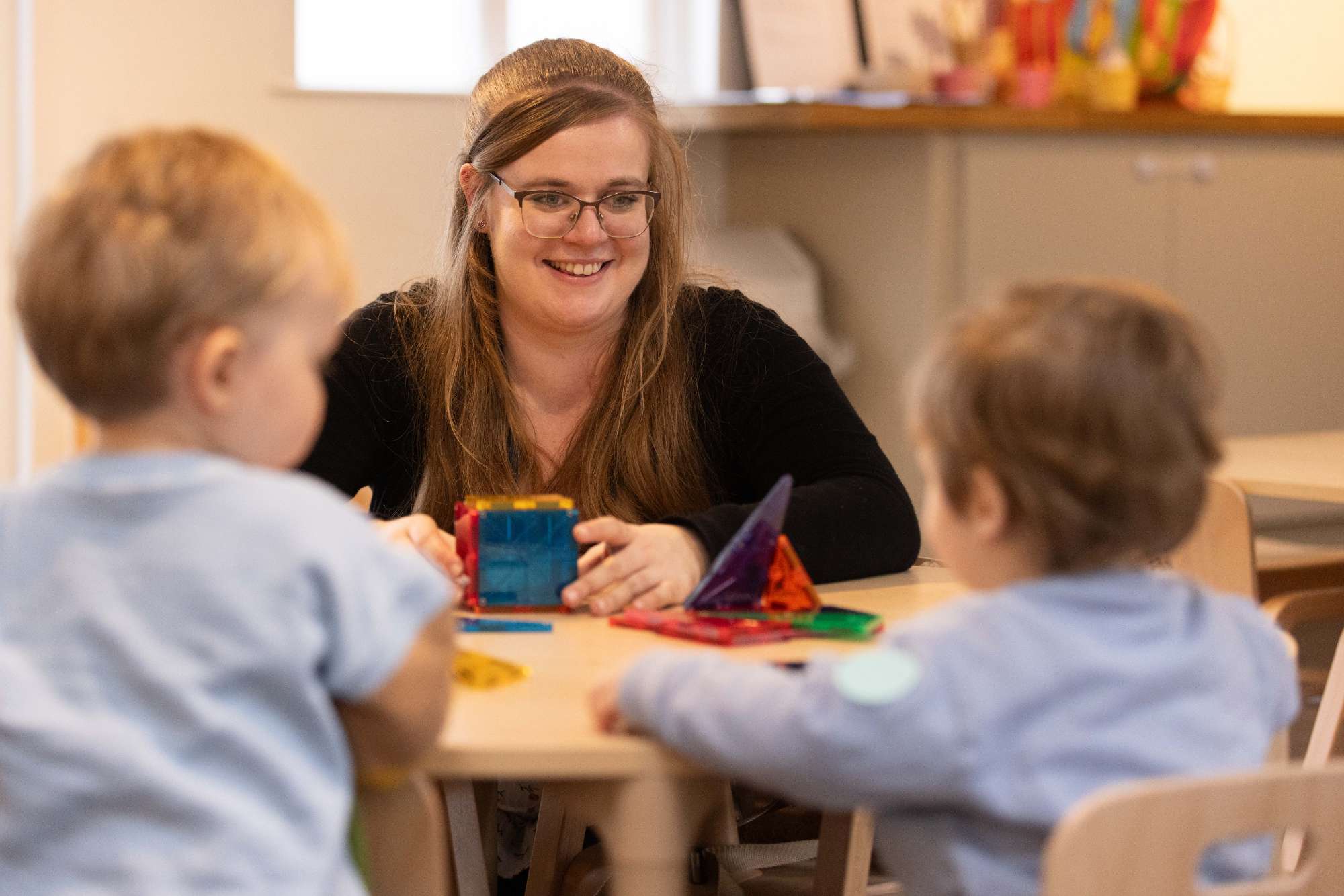 A nursery practitioner playing with magnetic tiles alongside two children
