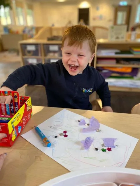 A nursery child smiling while drawing and crafting with crayons
