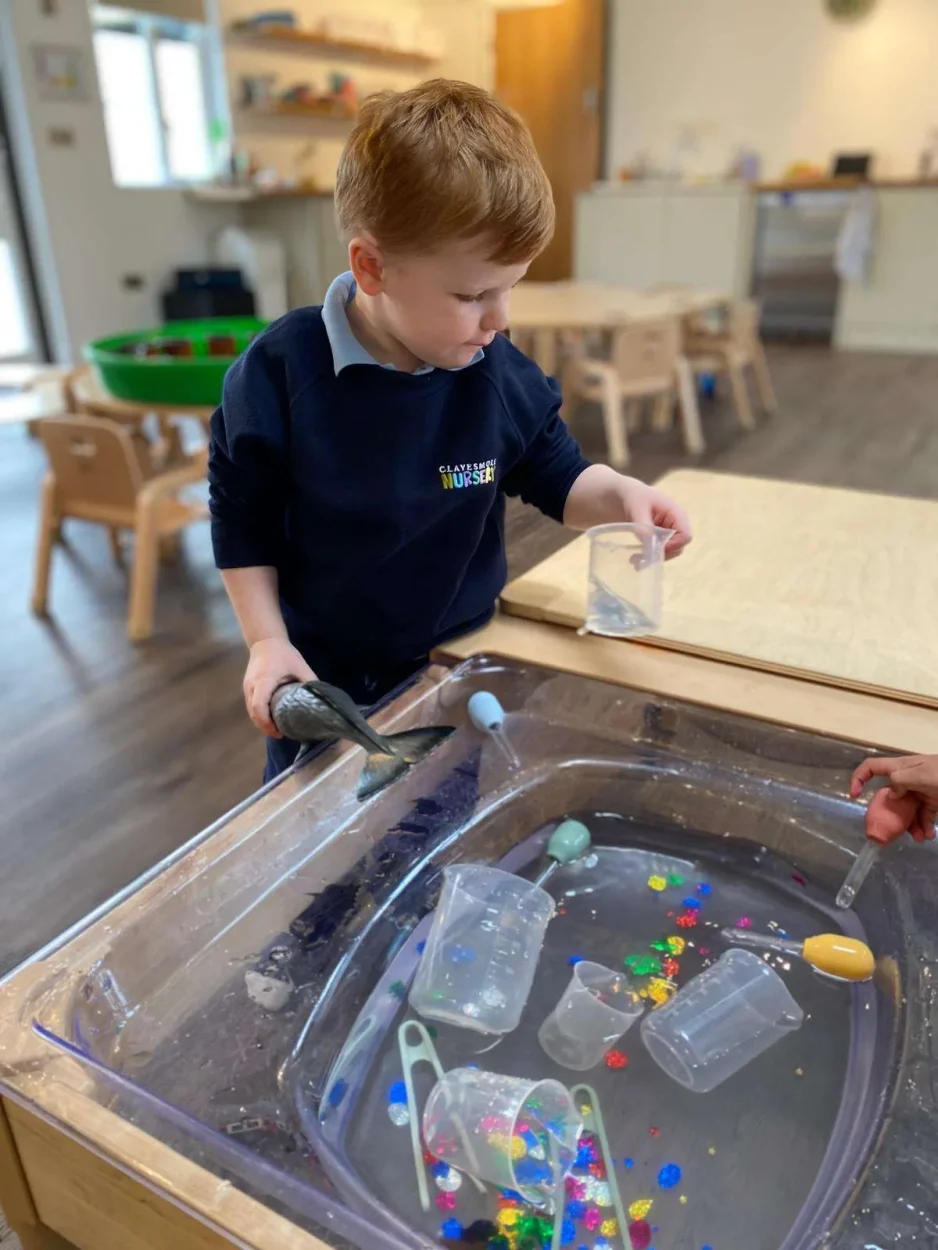A nursery child exploring a water play tray with cups and jugs