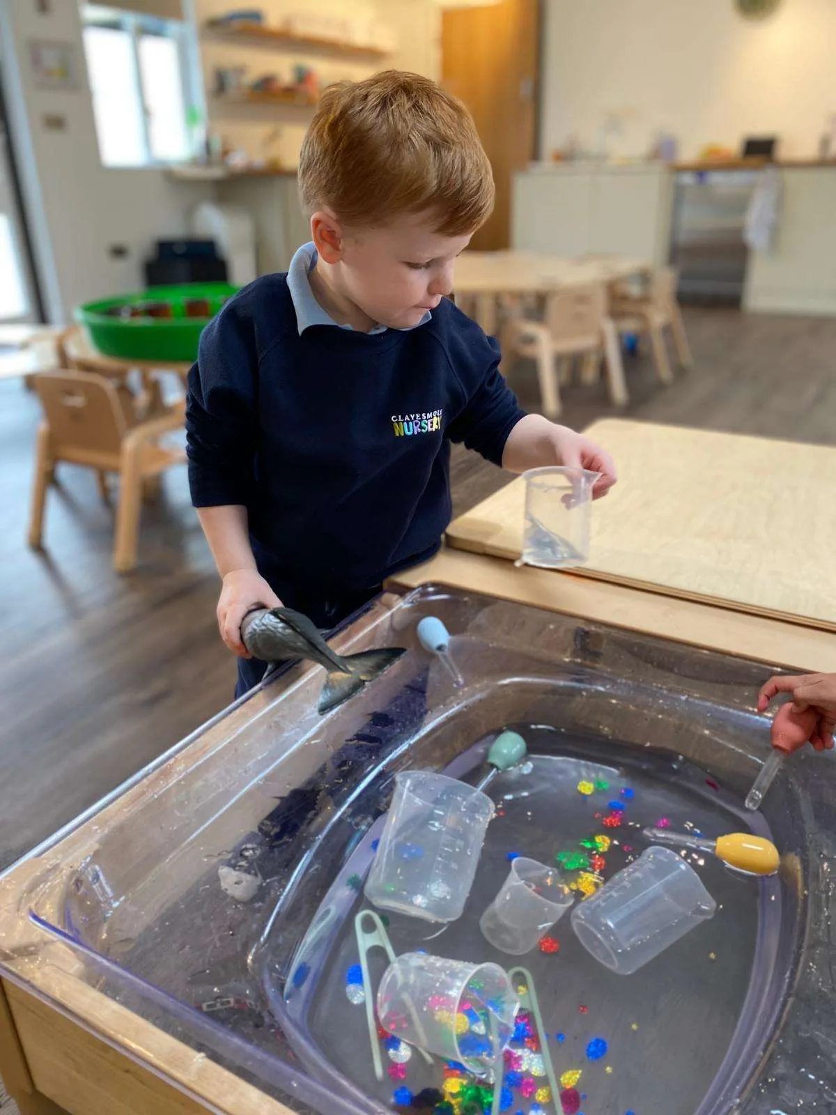 A nursery child exploring a water play tray with cups and jugs