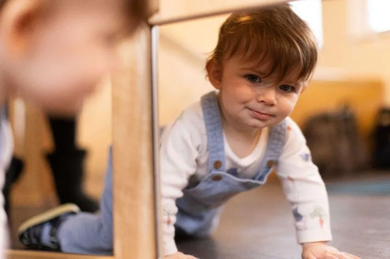 Baby in dungarees crawling beside a mirror in the nursery